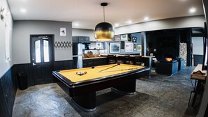 A billiards table in a room with a stone floor, a black door, and a fireplace.