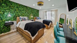 Quarto com duas camas, televisão, escrivaninha e parede verde.