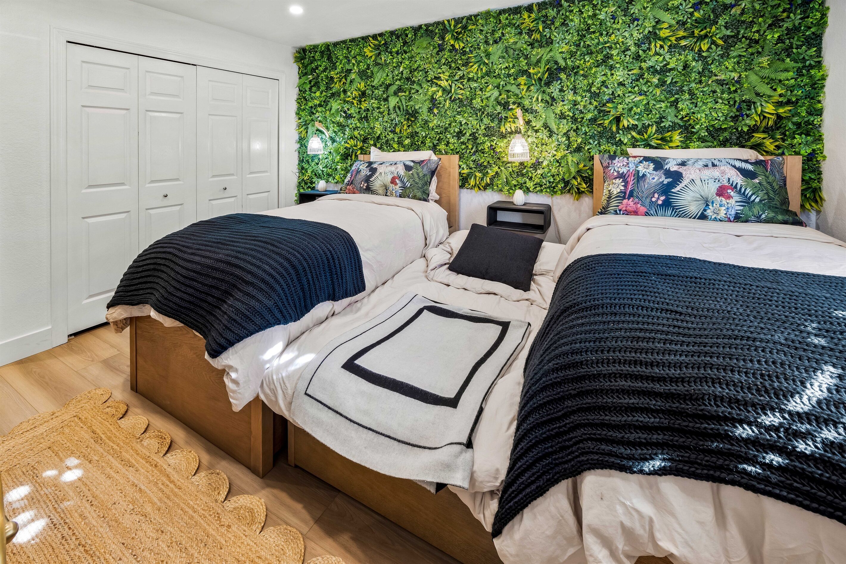 Une chambre avec deux lits, un mur recouvert de plantes vertes, une armoire blanche et un tapis tissé.