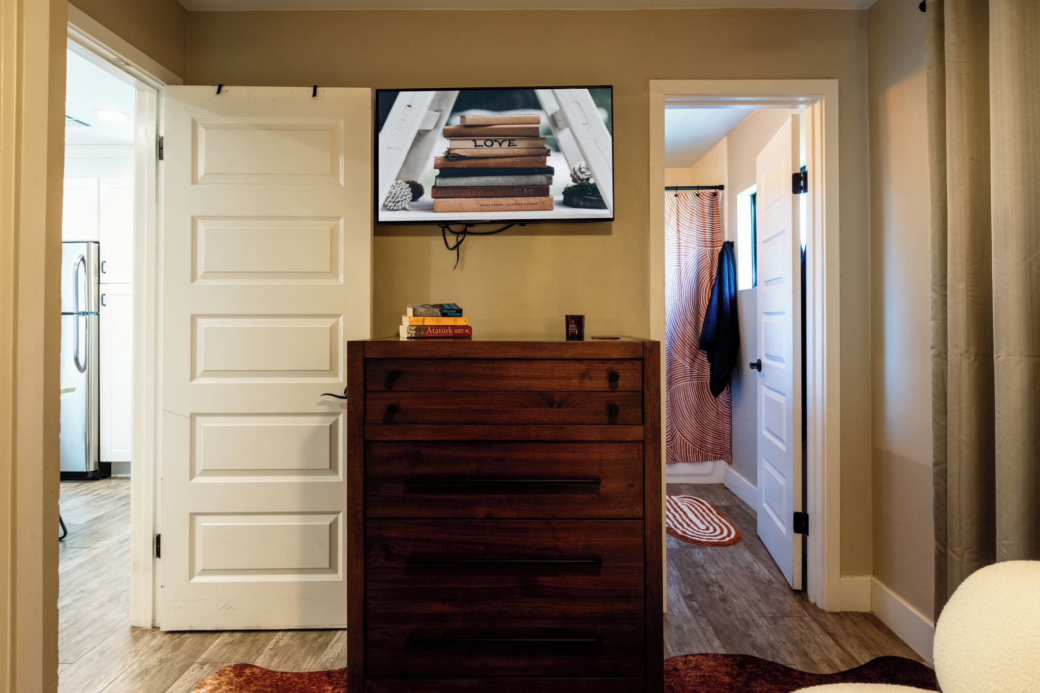 A hallway with a wooden cabinet, a television mounted above it displaying books, and a door leading to another room.