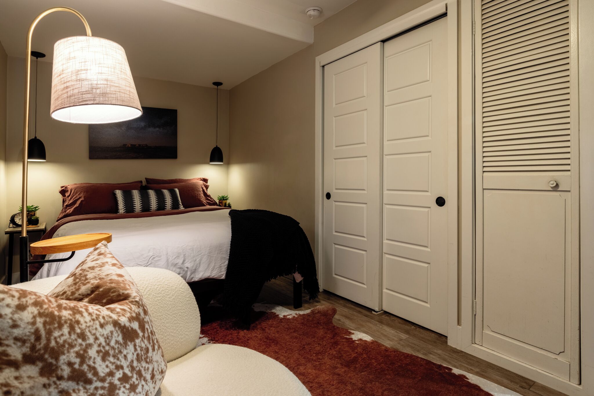 Un dormitorio con cama, mesita de noche, lámpara, puerta y alfombra roja.