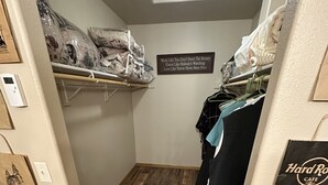 A narrow hallway with wooden flooring, a coat rack with clothes, a sign on the wall, and a Hard Rock Cafe bag on the right.