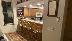 A compact kitchen with wooden cabinets, a microwave, and a bar area with four stools.