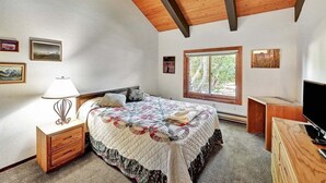 Ein Schlafzimmer mit Holzboden, einem Bett mit Decke, einem Nachttisch, einer Lampe, einer Kommode und einem Fernseher.