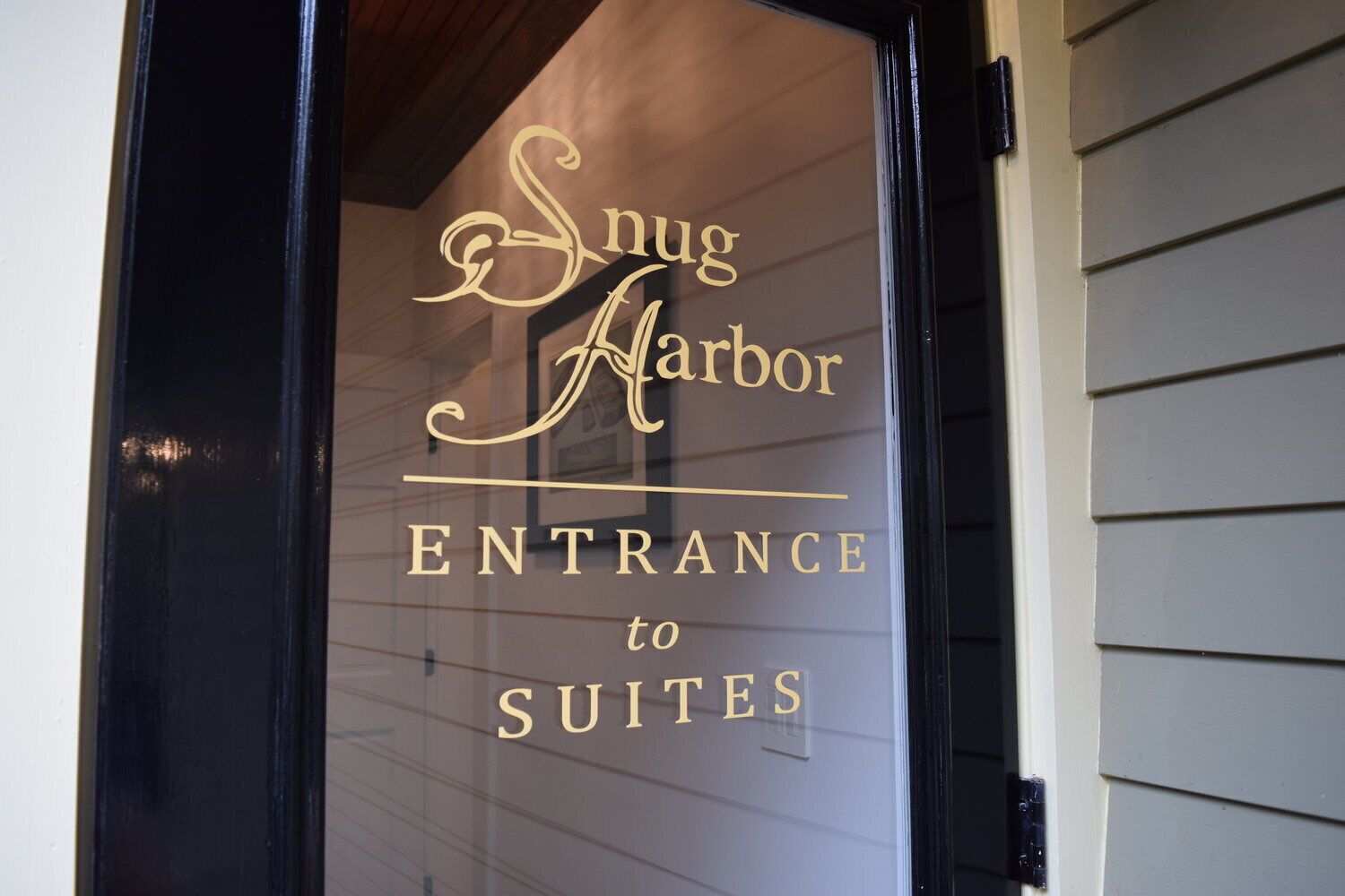 Een glazen deur met de tekst 'Snug Harbor Entrance to Suites' in gouden letters.
