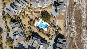 Oversigtsbillede af et boligområde med en central swimmingpool omgivet af huse, veje og grønt.