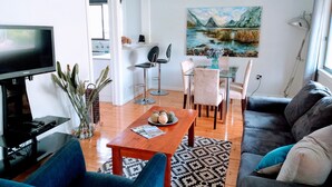 Un soggiorno moderno con una TV a schermo piatto, un divano, un tavolino da caffè e un'area pranzo con sedie e un quadro.