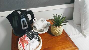 Een houten bijzettafeltje met een zwarte koffiezetapparaat, een witte mok, een ananas en een mandje met koffieporties.