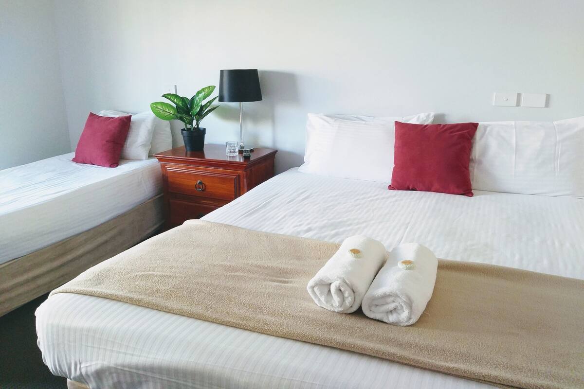 Ein Hotelzimmer mit zwei Einzelbetten, einem Nachttisch mit Lampe, einer Zimmerpflanze und einem beigen Handtuch auf dem Bett.