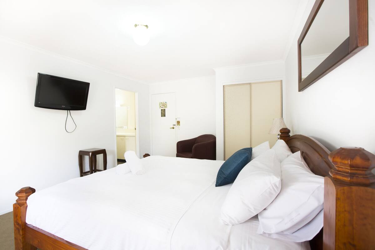 Ein Hotelzimmer mit einem großen Bett, einem flachbildfernseher an der Wand, einem Holz-Kopfteil und einem Spiegel.