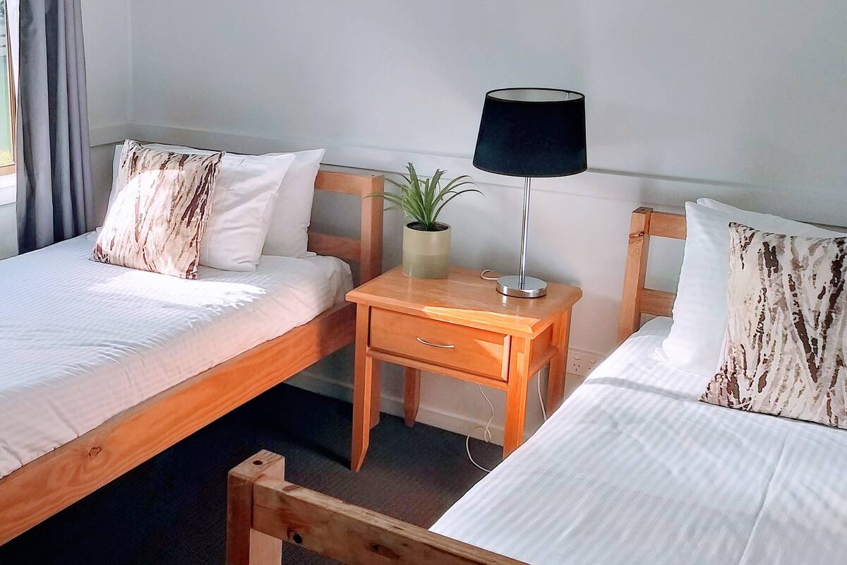 Ein Hotelzimmer mit zwei hölzernen Betten, einem kleinen Nachttisch mit Lampe und einem Blumentopf.