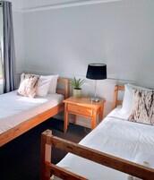 Habitación de hotel con dos camas de madera, una mesita de noche de madera con una lámpara y una planta en maceta.