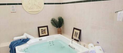Une salle de bain avec une grande baignoire, un porte-serviettes avec des serviettes, une œuvre d’art encadrée et une plante en pot.