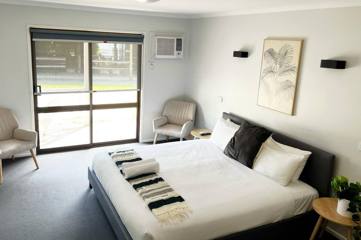 Ein modernes Hotelzimmer mit einem großen Bett, einem Sessel, einem kleinen Tisch und einer Topfpflanze.