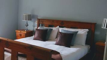 A wooden bed with a headboard, a bedside table, a lamp, and a wall-mounted air conditioner.