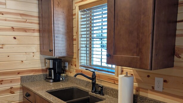 A kitchen with wooden cabinets, granite countertops, a sink, a coffee maker, and a window with blinds. - Peaceful Cabin for Two - Stunning Mountain Views - Wildlife Viewing (Gardiner)