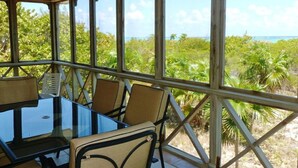 A room with a glass table and chairs, large windows, and a view of a tropical landscape. - Chill Out, Relax And Reconnect In A Sweet Cottage By The Beach (Whitby)