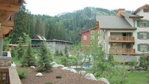 Un edificio a più piani con balconi, circondato da alberi e con montagne sullo sfondo.