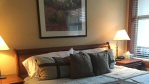 Un letto ben rifatto con una testiera in legno, una lampada da comodino e un quadro appeso al muro.