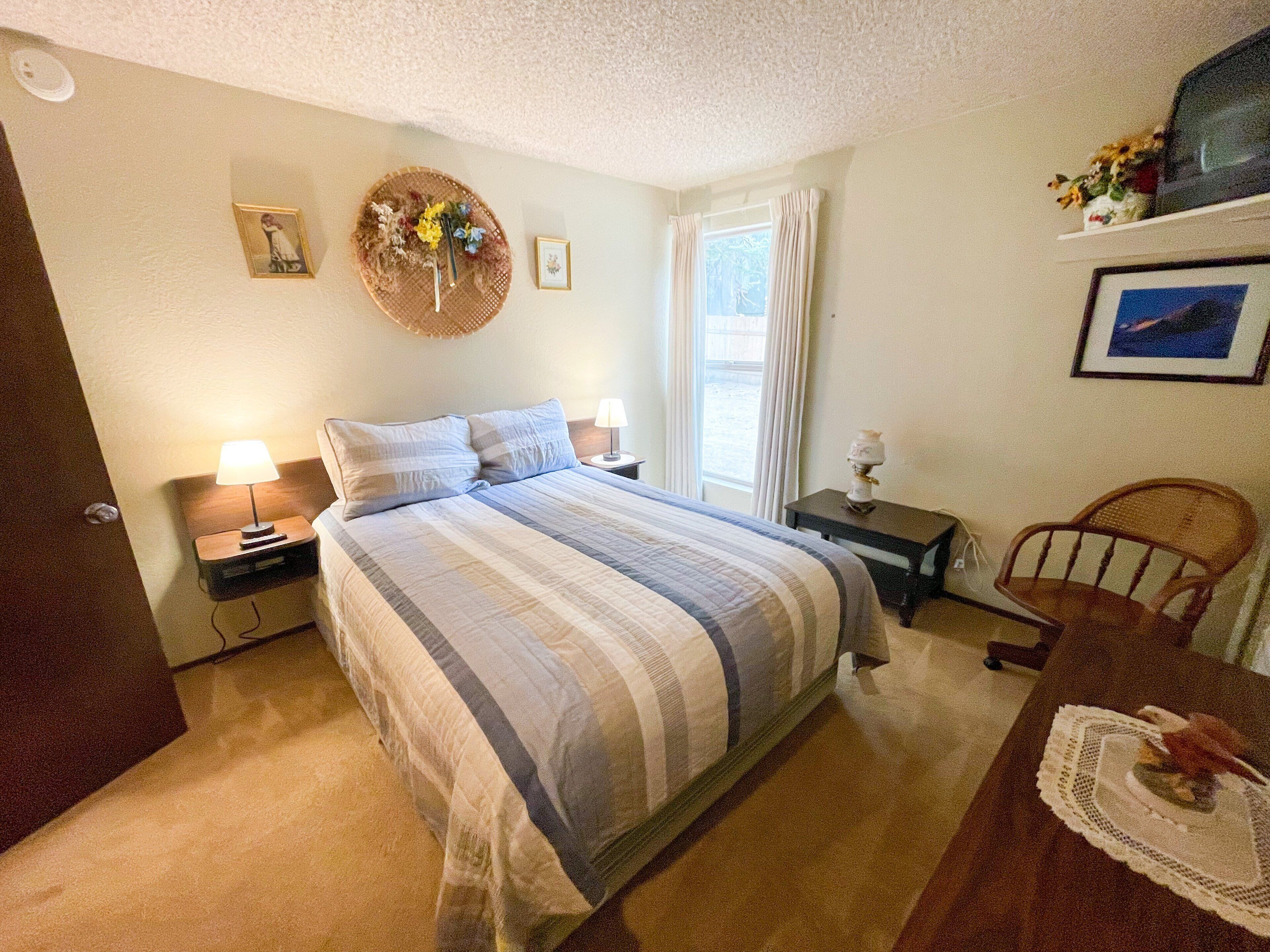 A neatly arranged bedroom with a large bed, two bedside tables, a wooden chair, and a small table with a vase.