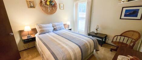 A neatly arranged bedroom with a large bed, two bedside tables, a wooden chair, and a small table with a vase.