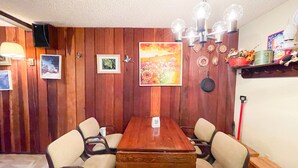 Ein Essbereich mit Holztisch und Stühlen, einer Chandelierleuchtre und Wanddekorationen, darunter gerahmte Bilder und ein Gemälde.