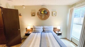 Ein Schlafzimmer mit einem großen Bett, zwei Nachttischen mit Lampen, einem Holzschrank und einer Wand, die mit einem runden Gewebekunstwerk und gerahmten Bildern geschmückt ist.