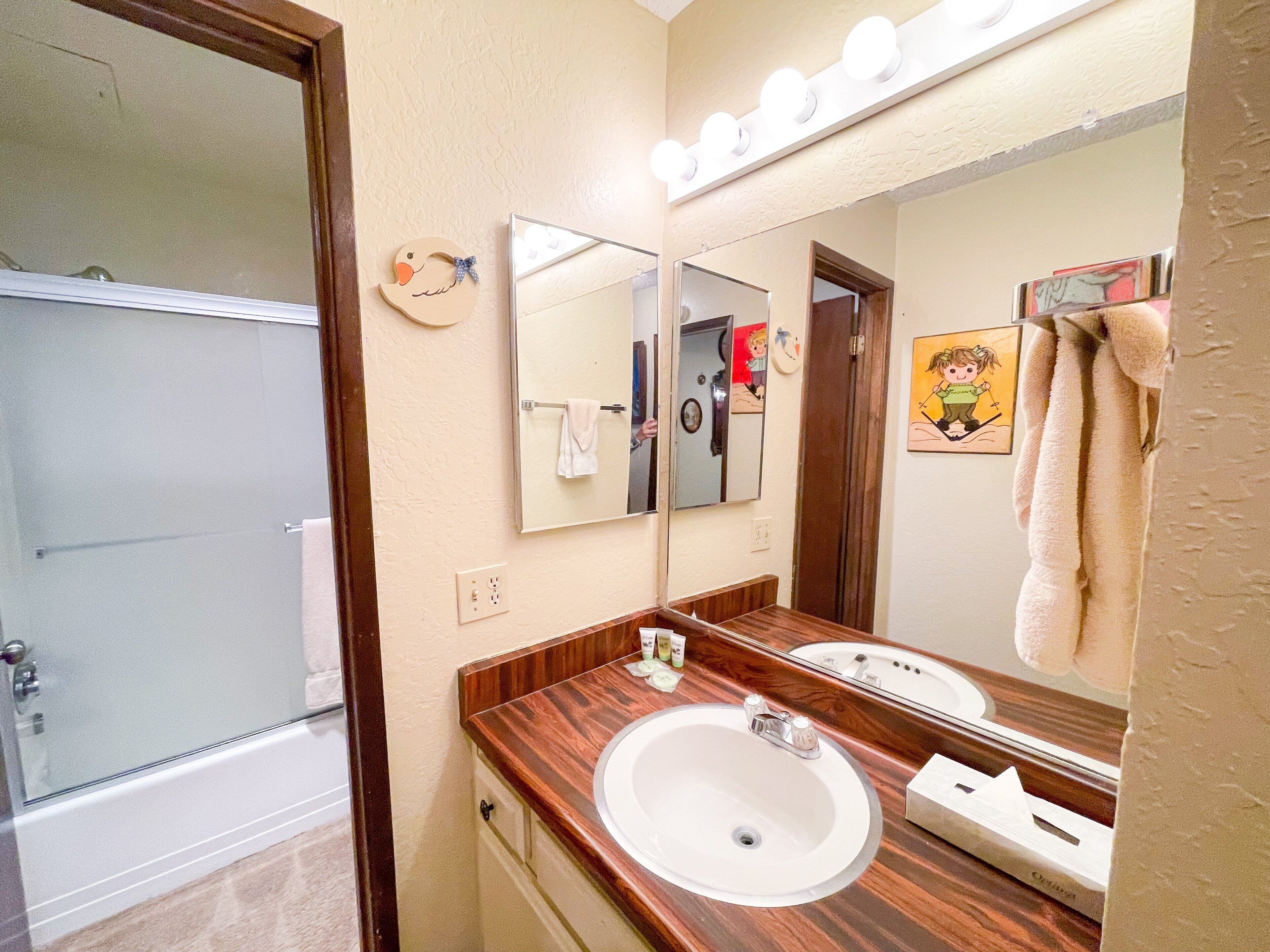 Une salle de bain avec un meuble-lavabo en bois, deux vasques, un grand miroir et un espace douche.