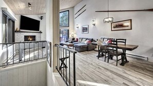 A spacious living room with a fireplace, a dining area with a wooden table and chairs, and a large window providing natural light. - Woodlands 31: Pet Friendly, On Sierra Star Golf Co (Mammoth Lakes)