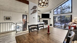 A spacious living area with a large wooden dining table, a fireplace, and a large window offering a view of the outdoors. - Woodlands 31: Pet Friendly, On Sierra Star Golf Co (Mammoth Lakes)