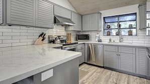 A modern kitchen with grey cabinetry, a stainless steel dishwasher, and a window with decorative items. - Woodlands 31: Pet Friendly, On Sierra Star Golf Co (Mammoth Lakes)
