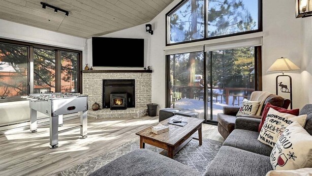 A spacious living room with a fireplace, a foosball table, and a large window overlooking a snowy landscape. - Woodlands 31: Pet Friendly, On Sierra Star Golf Co (Mammoth Lakes)