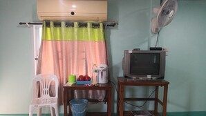 A room with a ceiling fan, a television on a wooden stand, a plastic chair, a table with a basket, and a window with a curtain. - Phakdeehome Viewmorg (Khao Kho)