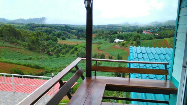 A balcony with a wooden bench and a view of a green landscape with fields and houses. - Phakdeehome Viewmorg (Khao Kho)