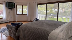 A bedroom with a large bed, a TV mounted on the wall, and a view of a balcony with a railing.