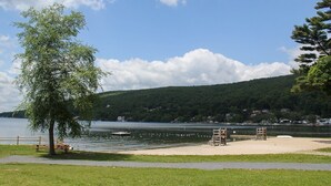 A lakeside park with picnic tables, a wooden deck, and a sandy area with benches.