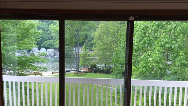 A view from a room with a sliding glass door to a deck overlooking a lake with houses in the background.