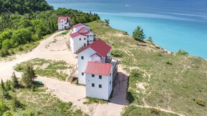 Una propiedad costera con varias edificaciones blancas con techos rojos, ubicada en una colina cubierta de hierba con vistas a un mar azul cristalino.