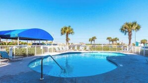Una piscina con un ombrellone blu, palme e un'area recintata con lettini.