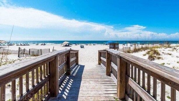 Una passerella di legno che conduce a una spiaggia sotto un cielo sereno.