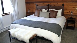 Ein Schlafzimmer mit einem Holzkopfteil, einem großen Bett mit weißer Bettwäsche, einem Fellüberwurf und zwei Nachttischen mit Lampen.