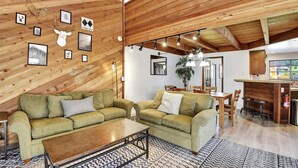 Ein gemütliches Wohnzimmer mit Holzboden, einem grünen Sofagarnitur, einem Couchtisch und einem gemusterten Teppich.