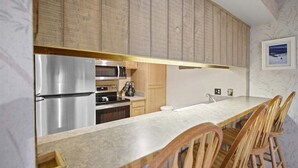 A modern kitchen with a stainless steel refrigerator, a microwave, and a coffee maker. There are wooden chairs and a long countertop. - Sunshine Village 165- Centrally Located, Near Eagl (Mammoth Lakes)