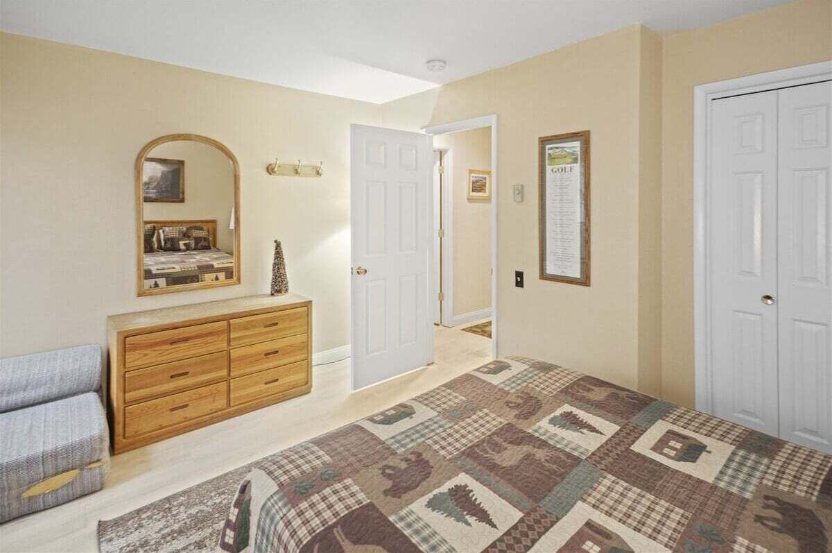 A bedroom with a bed, dresser, mirror, and a door leading to another room.