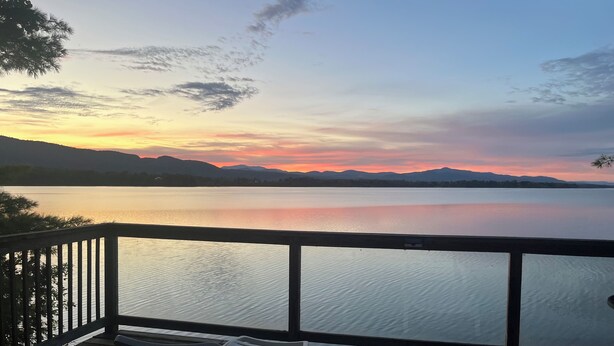 Eine Terrasse mit Stühlen mit Blick auf einen ruhigen See bei Sonnenuntergang.