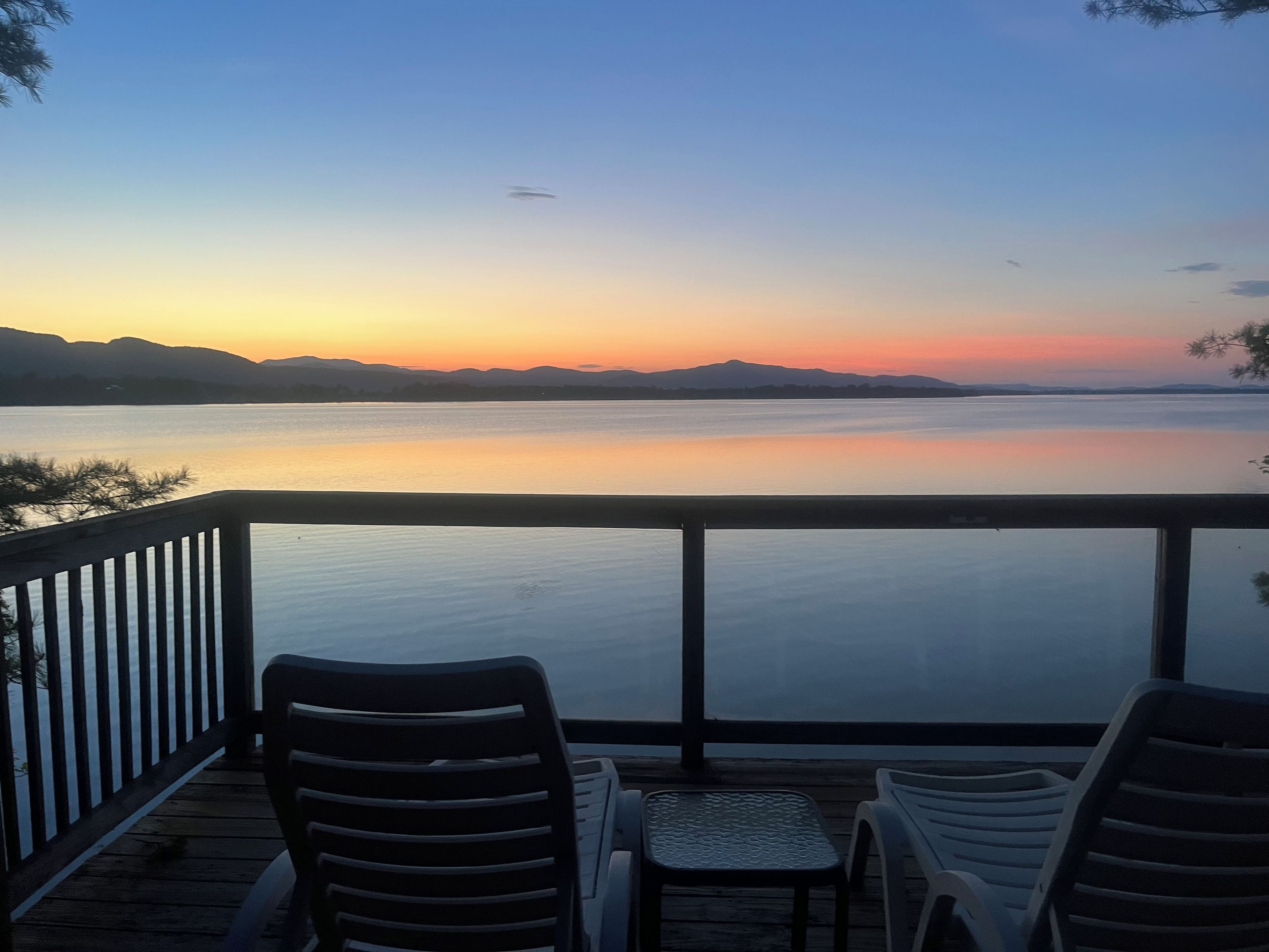 Terraza con dos sillas y una mesa frente a una masa de agua tranquila al atardecer.