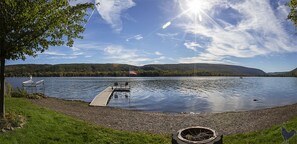 A lakeside view with a dock, a flag, and a chair. - Modern Lakefront home with wonderful views and plenty of space! (Honeoye)
