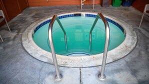 Ein kleiner, runder Pool mit Metallleitern, umgeben von einer Betonplattform.