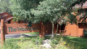 Ein Holzschild mit der Aufschrift "The Woodlands", umgeben von Grünpflanzen und einem kleinen Gebäude.