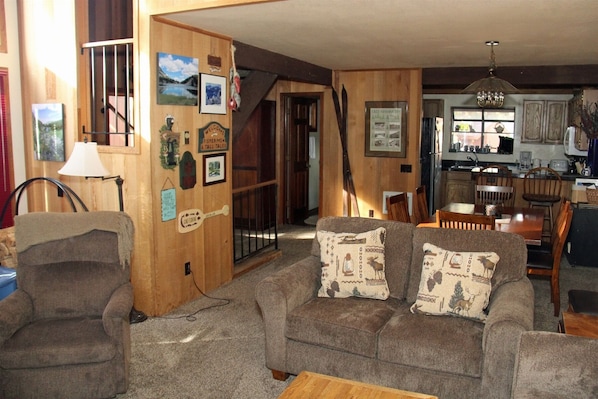 Un salon chaleureux avec un canapé, un fauteuil et un coin repas doté de meubles en bois.